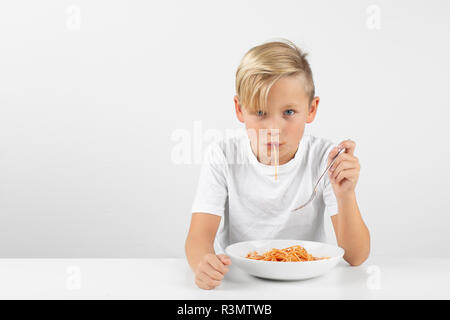 little blond boy in front of white background eats spaghetti and smiles Stock Photo