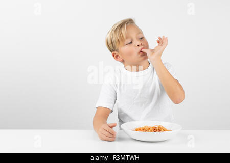 little blond boy in front of white background eats spaghetti and smiles Stock Photo