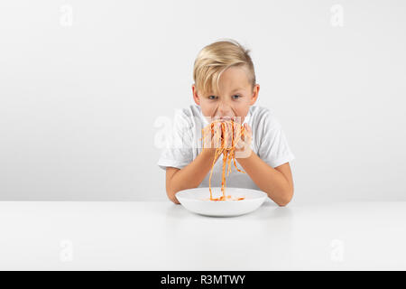 little blond boy in front of white background eats spaghetti with both hands and smiles Stock Photo