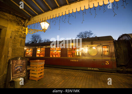 Heritage railway station at twilight, last train awaiting departure; third class, vintage carriages lit for last passengers of the day. Platform view. Stock Photo