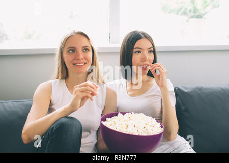 Women eating popcorn and watching tv Stock Photo