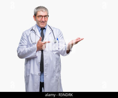 Handsome senior doctor man over isolated background amazed and smiling to the camera while presenting with hand and pointing with finger. Stock Photo