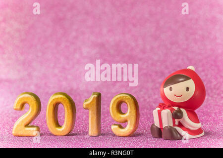 Pink glitter background for New Year's Cards with cute figurine of child in Christmas clothes with a present box in hands and handmade golden numbers  Stock Photo