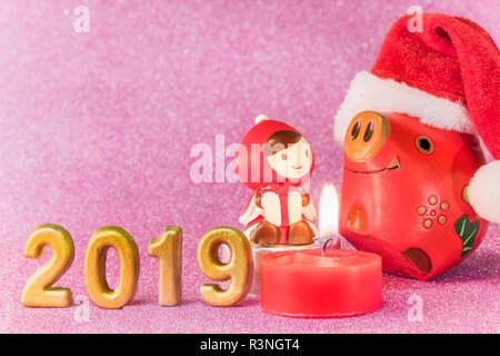 Pink glitter background for New Year's Cards with funny figurines of two boars  and chid with a Christmas hat dancing around a candle and handmade gol Stock Photo