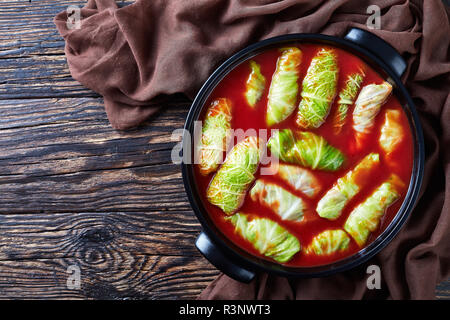 overhead view of raw cabbage leaves rolls stuffed with minced beef, boiled rice with tomato sauce in dutch oven on a n old rustic table, view from abo Stock Photo