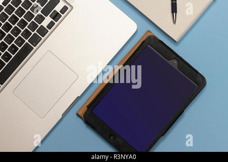 laptop computer, iPad mini and a note book on a blue desk, flat lay. Stock Photo