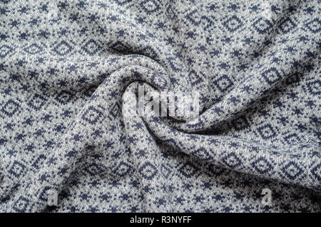 Crumpled background of gray winter sweaters with repeating geometric patterns and small snowflakes. Twisted in the center knitted fabric swatch Stock Photo