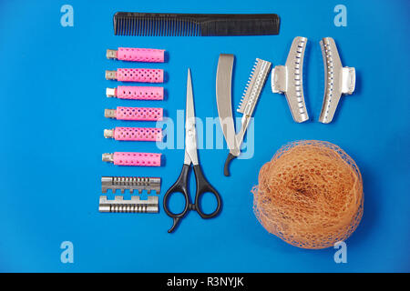 Flat lay with blue background of some of the tools of a hairdresser: tweezers, hairnets, curlers, combs, scissors and razor to cut the hair Stock Photo