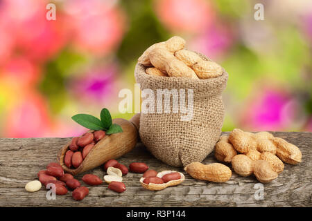 peanuts with leaf in bag on old wooden table with a blurry garden background Stock Photo