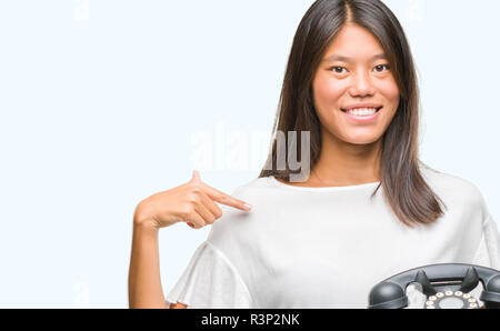 Young asian woman holding vintagera telephone over isolated background with surprise face pointing finger to himself Stock Photo