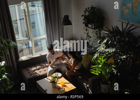 Man taking photo of woman having food with mobile phone in living room Stock Photo