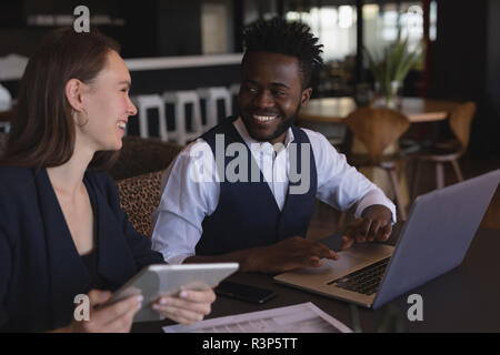 Business colleagues interacting with each other while using digital tablet and laptop Stock Photo