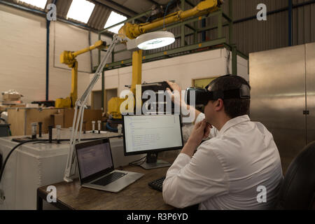Robotics engineer using virtual reality headset at desk Stock Photo