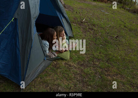 Couple using mobile phone in tent at campsite Stock Photo