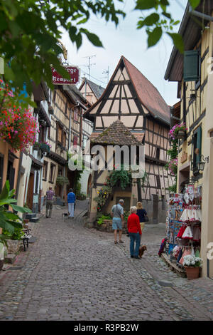 European Union, France, Alsace, Eguisheim village. Tourists walking along cobblestone street winding between traditional houses and shops. Stock Photo