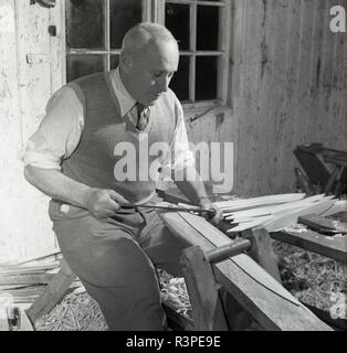 1950s, historical, a male craftsman in his workshop, using a tool to strip willow wood, England, UK. Basket weaving is an old, sacred tradition and was once an important skill in an age when containers were an indispensbale part of life. Stock Photo