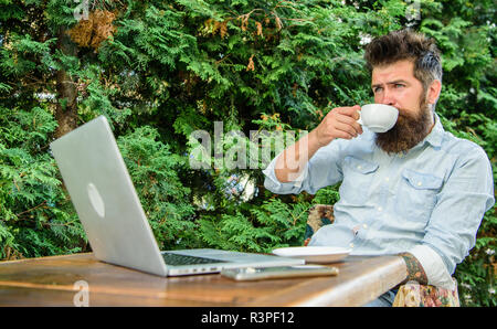 Guy drinks coffee relaxing terrace branches background. Aroma cappuccino. Pleasant moment. Man bearded hipster make pause for drink coffee and relax w Stock Photo