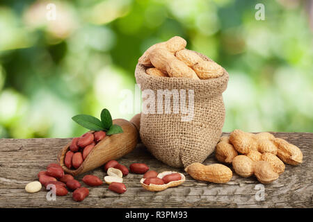 peanuts with leaf in bag on old wooden table with a blurry garden background Stock Photo