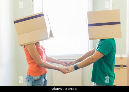 Couple with heads in cardboard boxes holding hands Stock Photo