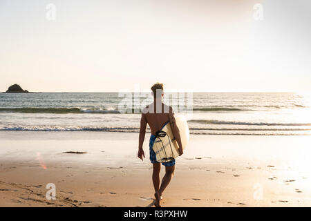 Young man walking on the beach, carrying his surfboard Stock Photo