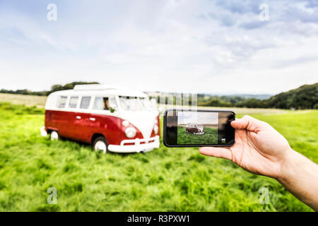 Woman's hand taking cell phone picture of van in rural landscape Stock Photo