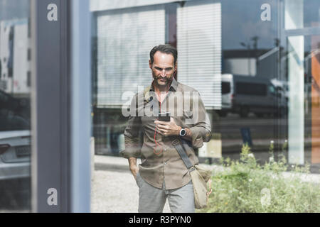 Smiling businessman using smartphone and earphones Stock Photo