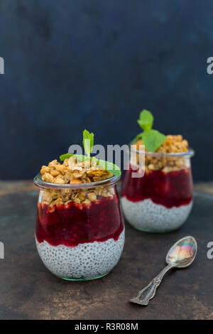 Two glasses of chia pudding with coconut milk, red fruit jelly and peanut granola topping Stock Photo