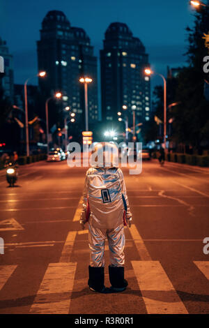 Rear view of spaceman standing on a street in the city at night Stock Photo