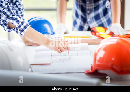 closeup hand of engineer manager point out with red pin point on construction blueprint on working table in construction site with safety helmet in pl Stock Photo