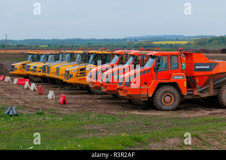 A line of articulated dump trucks are parked up in the yard before the start of shift on the construction of IPORT in Doncaster,South Yorkshire Stock Photo
