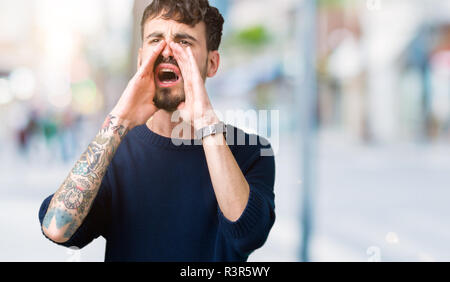 Young handsome man over isolated background Shouting angry out loud with hands over mouth Stock Photo