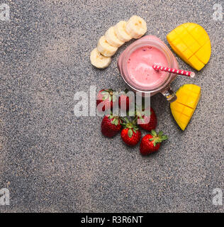 Fresh smoothies from ripe juicy fruit in a jar, around laid strawberries, mangoes, bananas, place for text, on a granite background, Superfoods and he Stock Photo