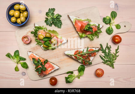 Sandwiches with salted red fish, cherry tomatoes, arugula, curd cheese and herbs, on a white wooden rustic background, space for text Stock Photo