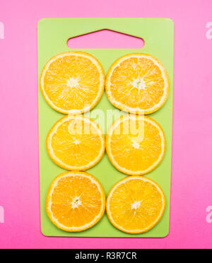Sliced appetizing oranges on a green cutting board and a bright pink background Stock Photo