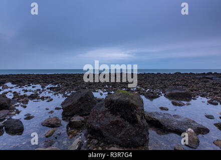 rocky and rugged foreshore on the coastline of the isle of wight in atmospheric and dramatic evening light at low tide. Stock Photo