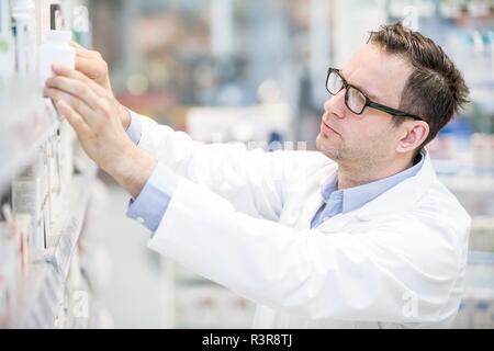 Male pharmacist looking for medicine on shelf in pharmacy. Stock Photo