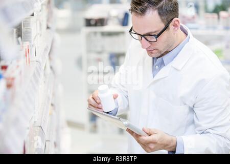 Male pharmacist using digital tablet to check pill bottle in pharmacy. Stock Photo