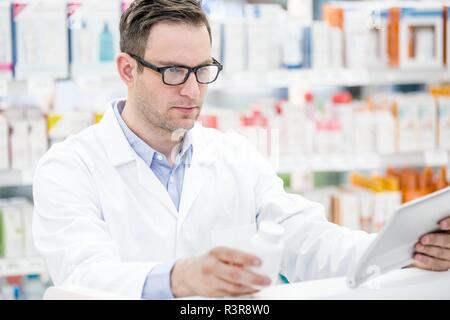 Young male pharmacist using digital tablet to check pill bottle in pharmacy. Stock Photo