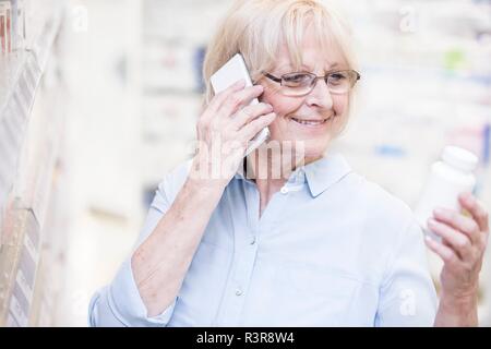 Senior woman discussing medicine on mobile phone in pharmacy. Stock Photo