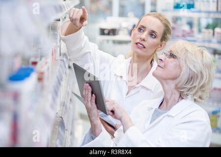 Female pharmacists checking medicines on shelf using digital tablet. Stock Photo