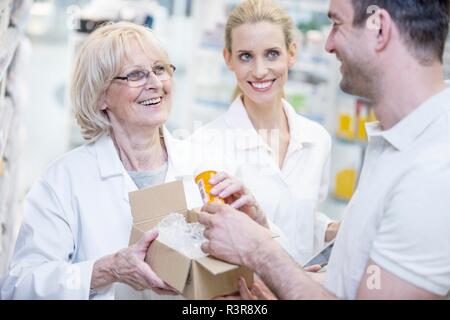 Pharmacist taking pill bottle from a box and giving it to customer. Stock Photo