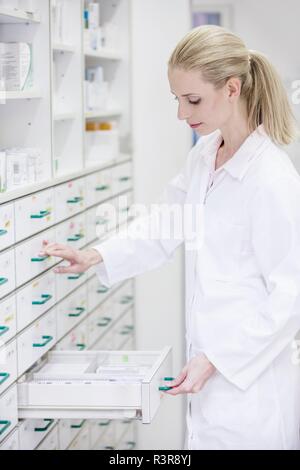 Female pharmacist looking for medicine in drawer cabinet in pharmacy. Stock Photo