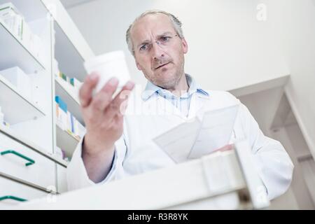 Male pharmacist reading label on pill bottle while looking for medicine in drawer cabinet in pharmacy. Stock Photo