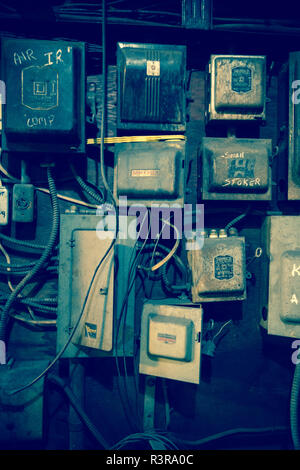 A jumble of electrical boxes and wires are mounted together on a wall, with a grungy feel Stock Photo