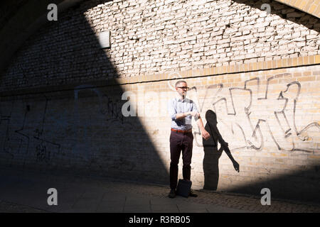 Businessman standing outdoors rolling up his sleeves Stock Photo