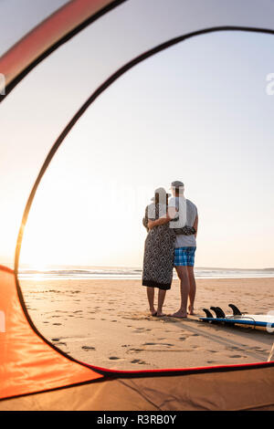 Romantic couple camping on the beach, embracing at sunset Stock Photo