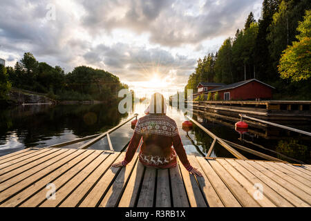 Finland, Kajaani, Man sitting on jetty, watching sunset, rear view Stock Photo