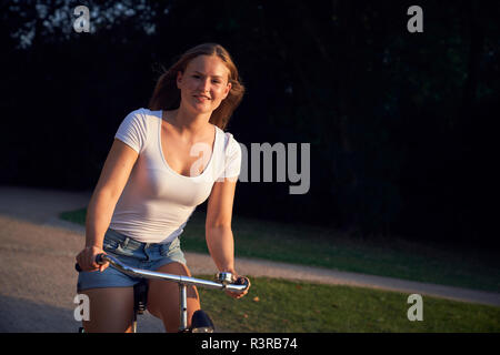 Cheerful young woman, riding bicycle in park Stock Photo