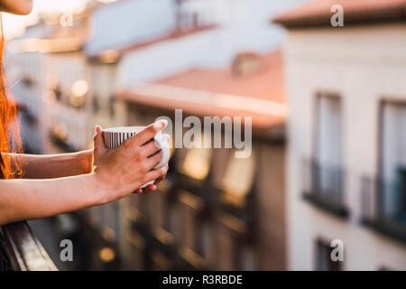 Hands of woman on balcony above the city at sunset holding cup of coffee Stock Photo