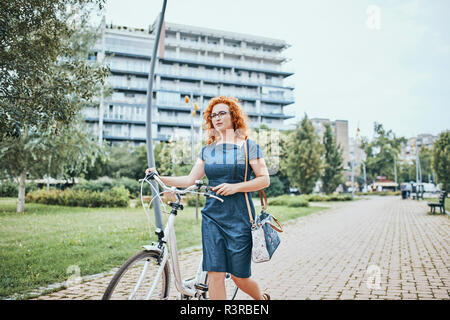 Young woman walking in park, pushing bicycle Stock Photo